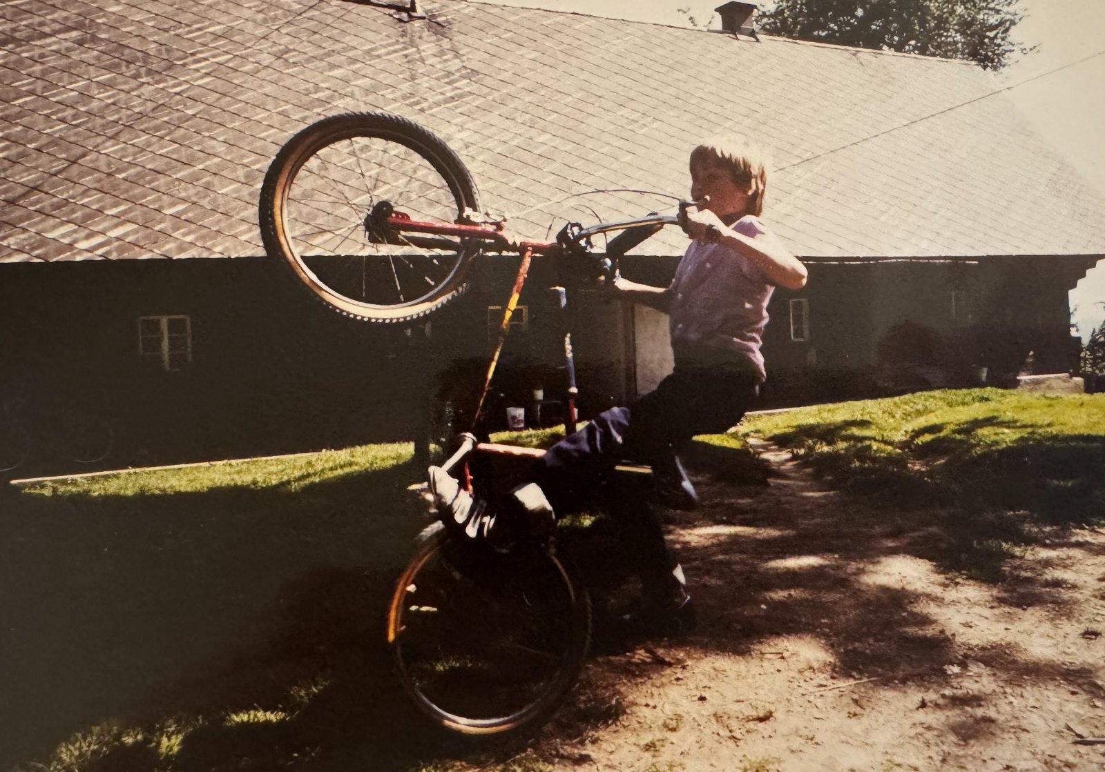 Christian hebt als Kind das Vorderrad seines BMX vor dem Bauernhaus